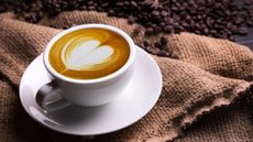A espresso with latte art on the top in a white coffee cup and saucer next to a hessian sack and coffee beans