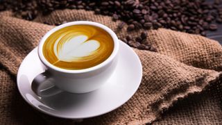 A espresso with latte art on the top in a white coffee cup and saucer next to a hessian sack and coffee beans